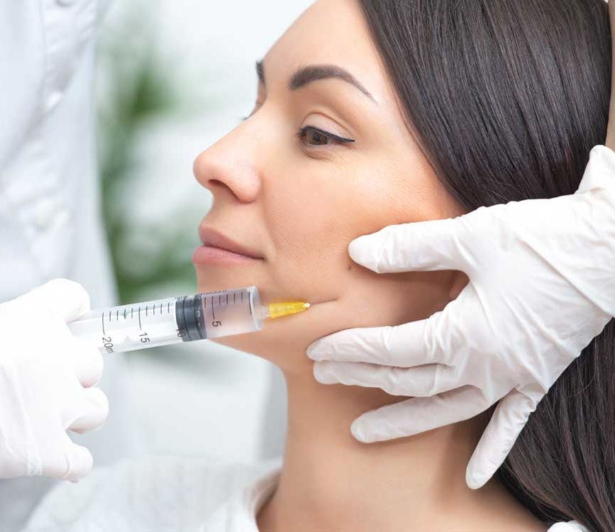 Dermal Fillers woman with brown hair getting face injected with syringe held by white gloved hands. Dermal Fillers